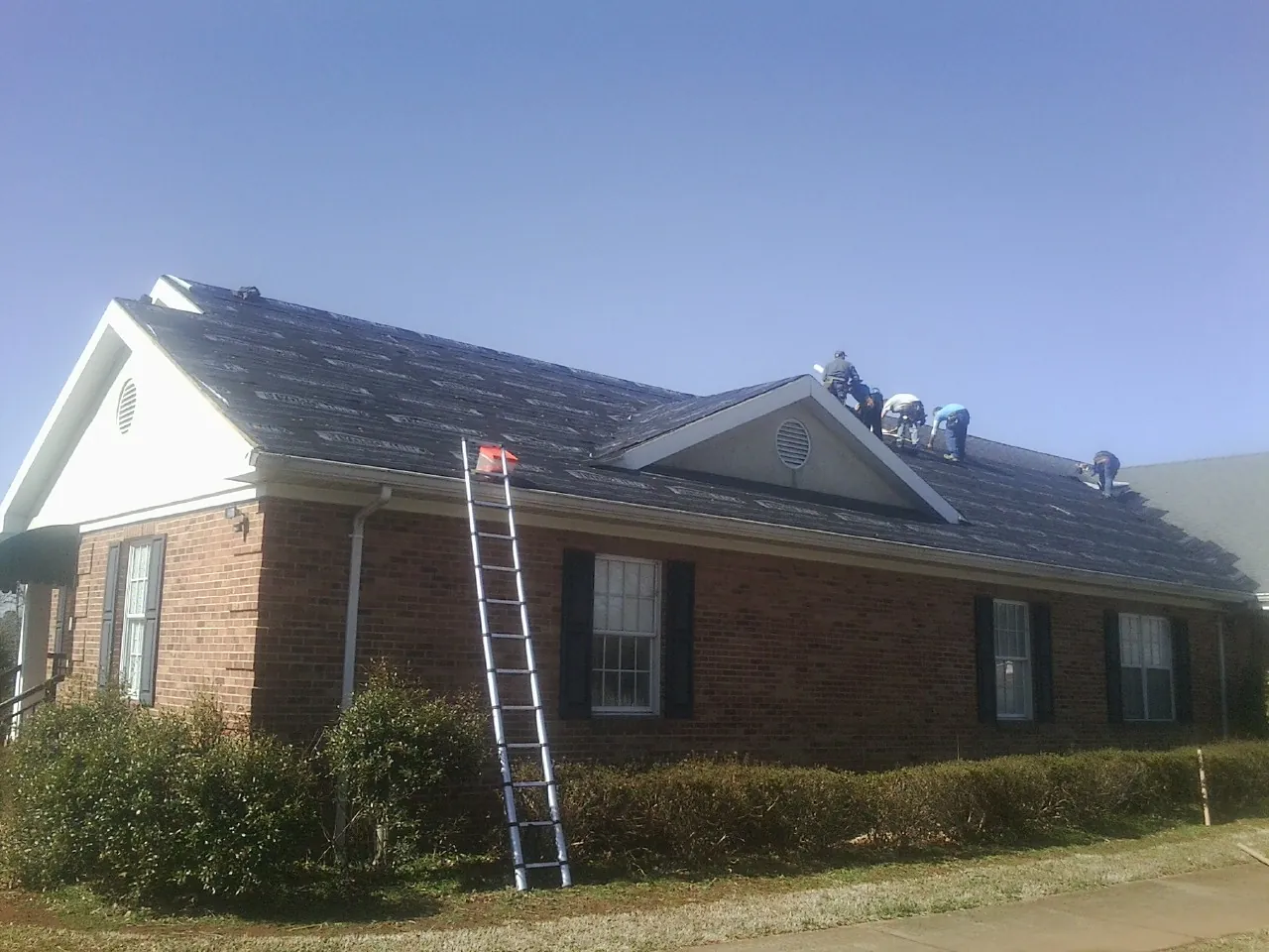 Crew tearing shingles off a brick ranch roof with a ladder set — Emergency Roof Repair work by our crew in Elberton
