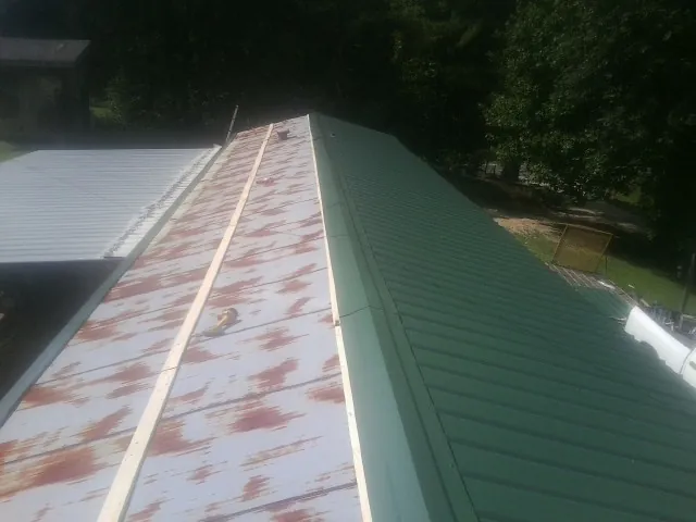 Old rusted panels beside newly installed green metal roofing — Wind Damage Roof Repair by Roofing Brothers in Elberton
