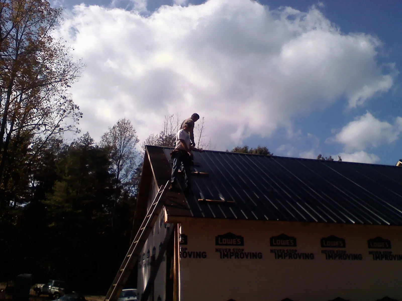 Roofer fastening dark metal panels high against a cloudy sky, from a Roof Inspection job in Elberton