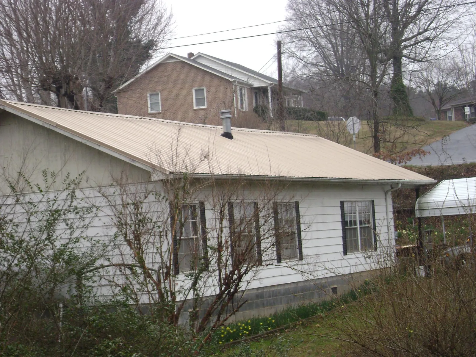 Tan metal roof on a white sided house set into a hillside — Commercial Roofing by Roofing Brothers in Elberton