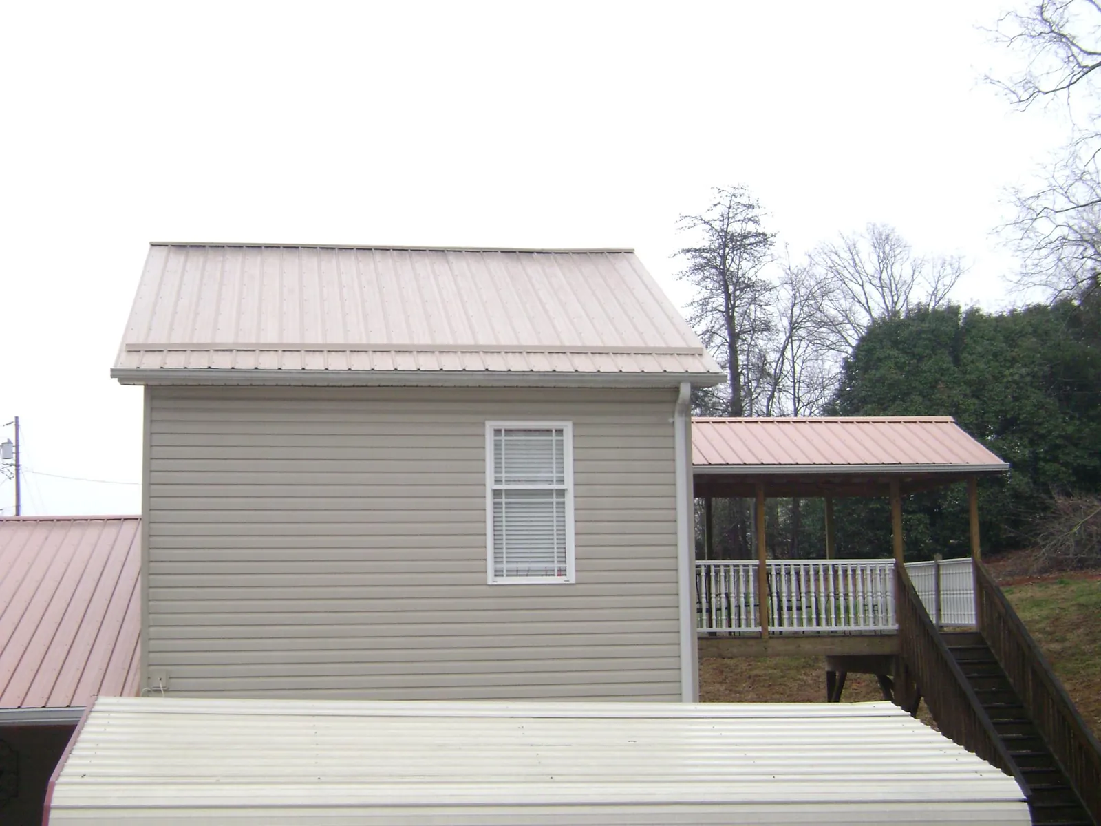 Tan metal roofs on a two story addition and attached porch, from a Roof Replacement job in Elberton